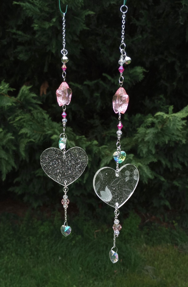 two almost identical sun catchers, both featuring a flat holographic heart and a pale pink star.