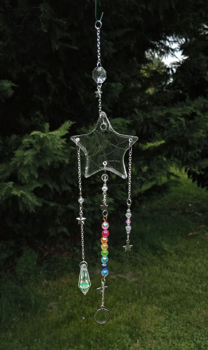 resin star with three strings hanging off of it. the middle has a string of rainbow beads and ends in a round resin disc. one side ends in a crystal pendant, and the other ends in a small metal star.