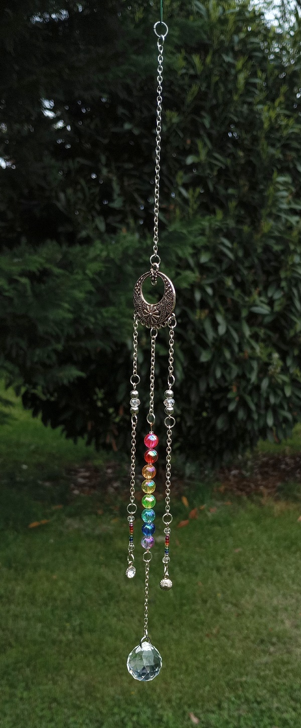 three strings of beads and chain hanging from a large cirular earing, making a sun catcher. the center string has rainbow beads, and also has a large teardrop shapped crystal at the bottom