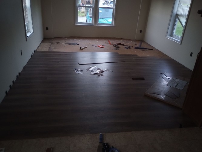 3/4s of a floor covered in vinyl plank, showing bare subfloor and scattered tools.