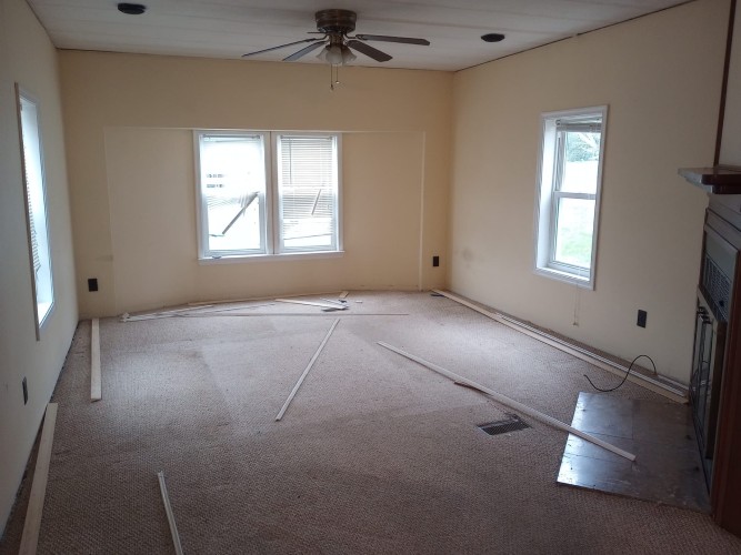 Small open living room with a bay window, a fireplace, dingy carpet, and white trim.