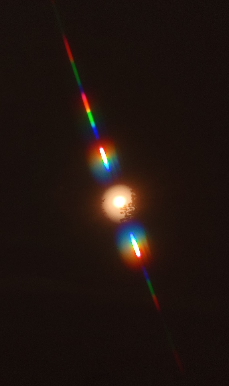 An orange sun captured through a small hole. Two rainbow streaks form a line across the hole.