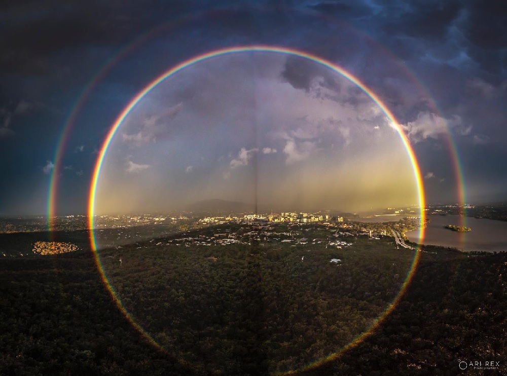 A full rainbow and its faint secondary viewed against a twilight sky and horizon.
