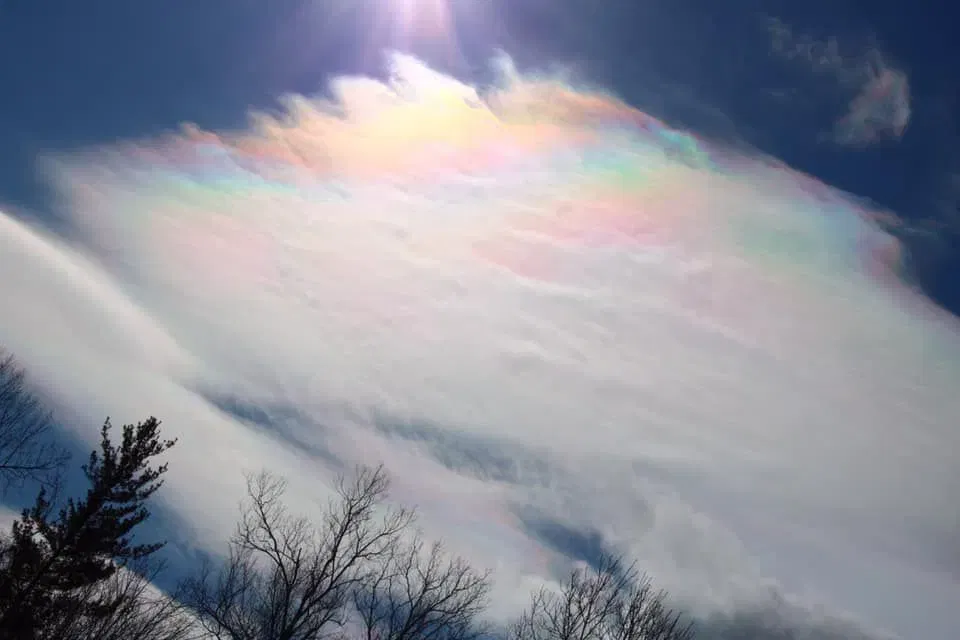 thin white cloud under the sun, its top taking on rainbow colored bands that become less even on its side further form the sun.