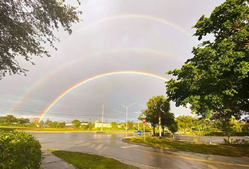 three rainbows above a rainy road intersection, flanked by trees
