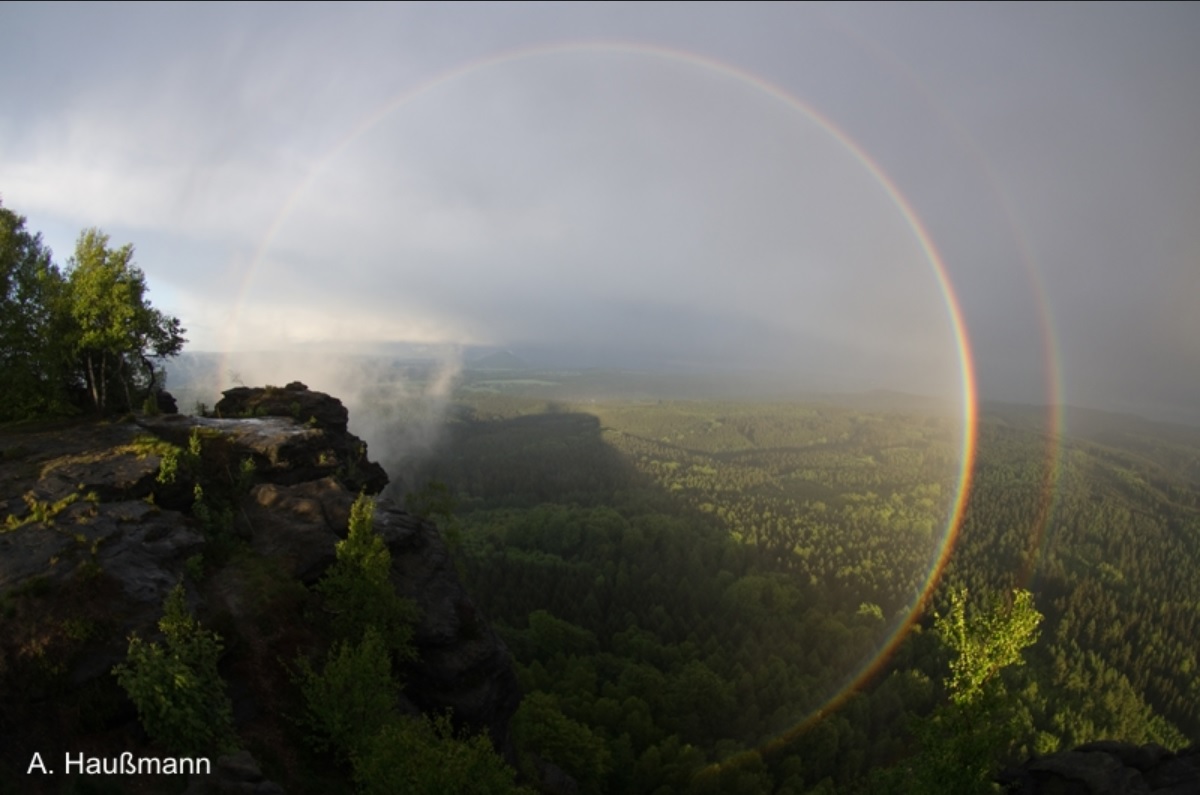 three fourths of a full rainbow, viewed from a lush mountain